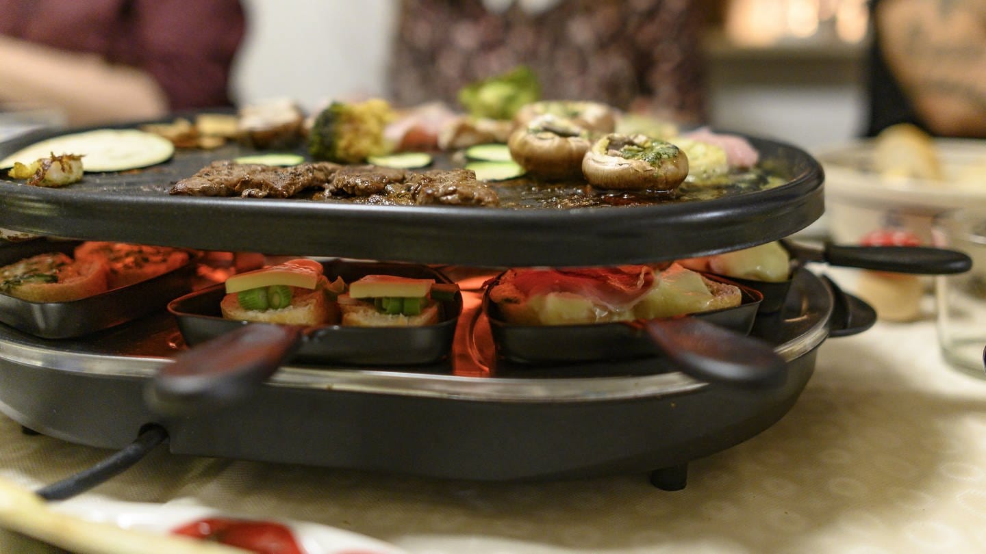 Ein Raclette-Gerät auf einem gedeckten Tisch (Foto: dpa Bildfunk, Picture Alliance)