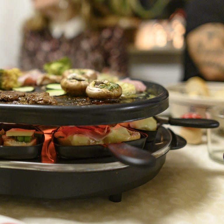 Ein Raclette-Gerät auf einem gedeckten Tisch  (Foto: dpa Bildfunk, Picture Alliance)