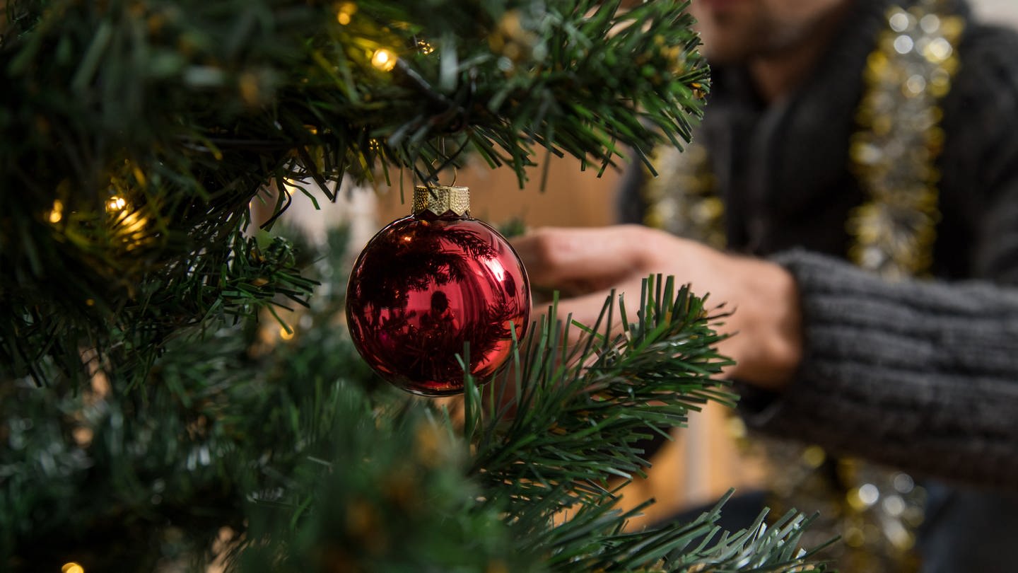 Ein Mann schmückt einen Weihnachtsbaum. (Foto: picture-alliance / Reportdienste, Picture Alliance)