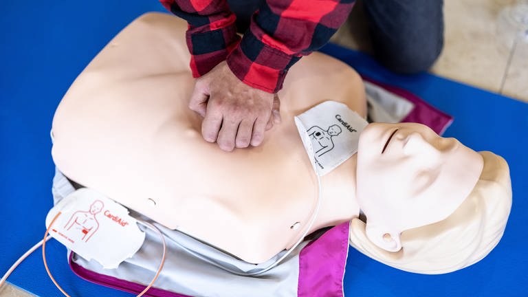 Ein Mensch übt eine Herzdruckmassage an einer Puppe.