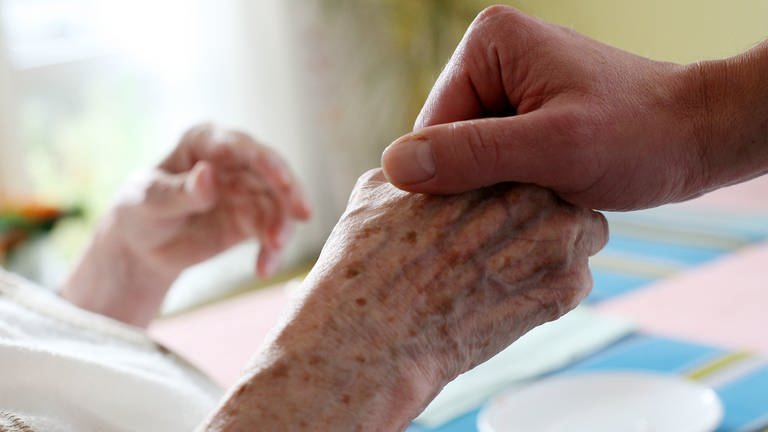 Eine pflegende Person hält die Hand eines alten Menschen