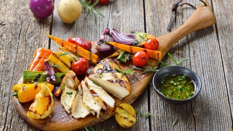 Grillgemüse und ein Hähnchensteak auf einem Holzbrett angerichtet