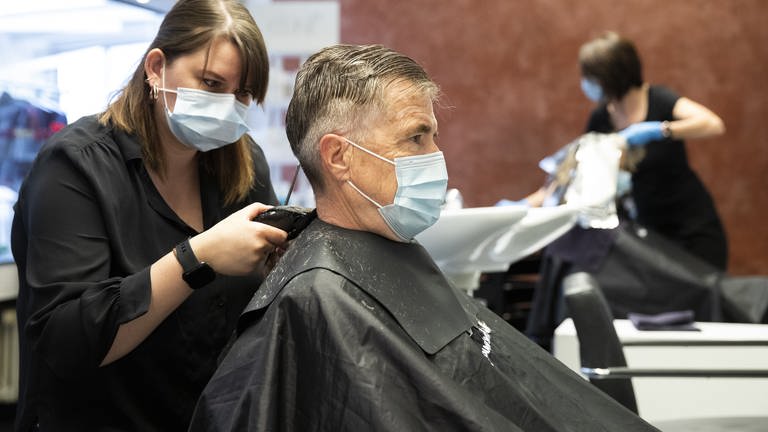 Eine Friseurin schneidet einem Kunden mit Schutzausrüstung die Haare (Foto: dpa Bildfunk, Picture Alliance)