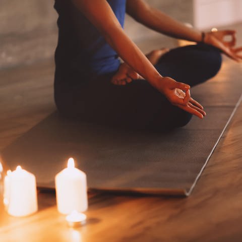 Eine Frau macht auf einer Matte eine Yoga übung im Schneidersitz. Neben ihr leuchten Kerzen (Foto: picture-alliance / Reportdienste, Dasha Petrenko)