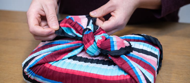 Eine Frau wickelt ein Geschenk mit der japanischen Furoshiki-Technik in ein Tuch ein  (Foto: picture-alliance / Reportdienste, Andrea Warnecke)