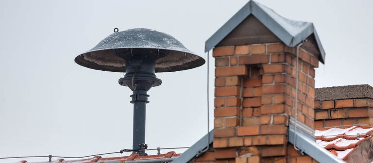 Eine Sirene ist neben einem Schornstein auf einem Hausdach montiert. Am bundesweiten Warntag kommen die Sirenen zum Einsatz. (Foto: picture-alliance / Reportdienste, picture alliance / ZB)