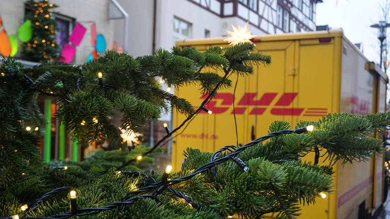 Ein Fahrzeug der DHL in einer Stadt, hinter einem Weihnachtsbaum.