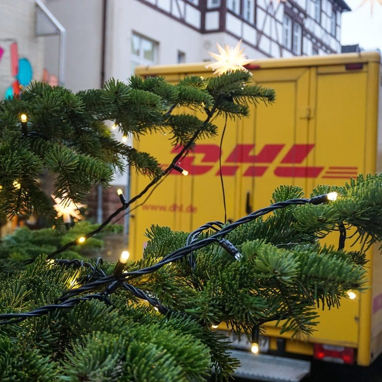 Ein Fahrzeug der DHL in einer Stadt, hinter einem Weihnachtsbaum.