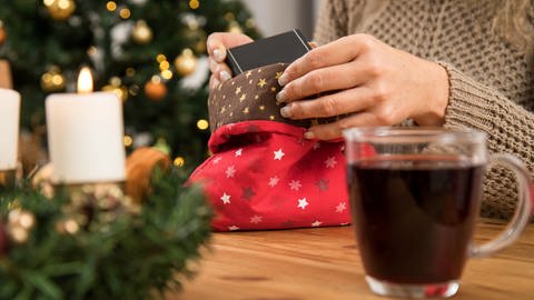 Eine Frau packt ein Weihnachtsgeschenk in einen Stoffbeutel ein. Man sieht nur ihre Hände. Der Beutel ist weihnachtlich bestickt (Foto: picture-alliance / Reportdienste, Christin Klose)