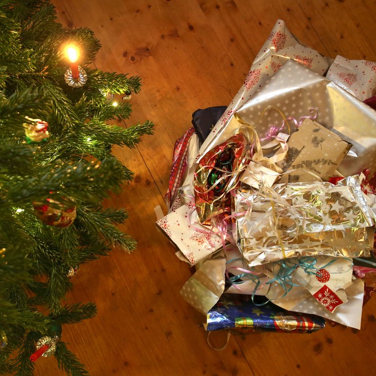 Zerknülltes Geschenkpapier liegt neben einem Weihnachtsbaum auf dem Boden