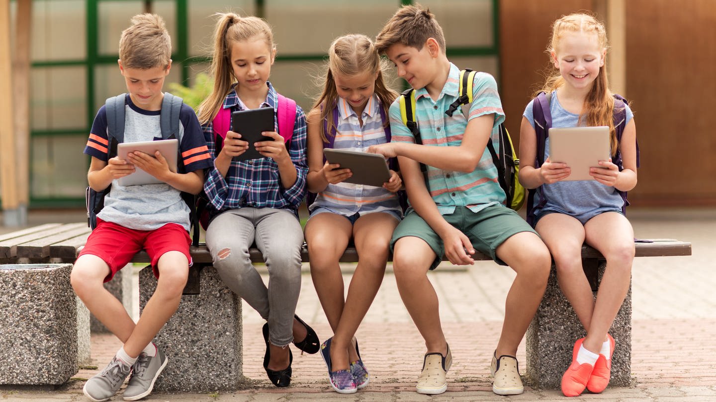 Fünf Schulkinder sitzen auf einer Bank und schauen auf ihre Tablets (Foto: picture-alliance / Reportdienste, picture alliance / Zoonar | lev dolgachov)