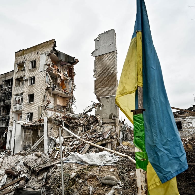 Eine ukrainische Flagge steht vor einem zerstörten Wohnhaus in Orikhiv, im Südosten der Ukraine. (Januar 2024) (Foto: picture-alliance / Reportdienste, picture alliance / Photoshot | Dmytro Smolienko / Avalon)