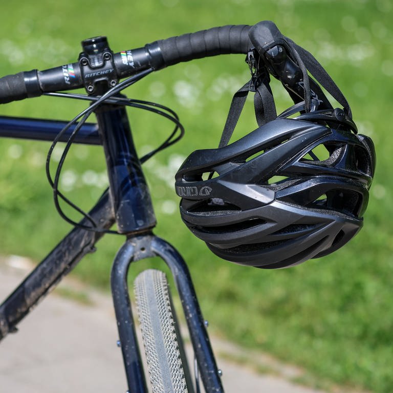 Ein Fahrradhelm hängt an einem Fahrradlenker | Darauf sollten Sie beim Kauf von Fahrradhelmen achten