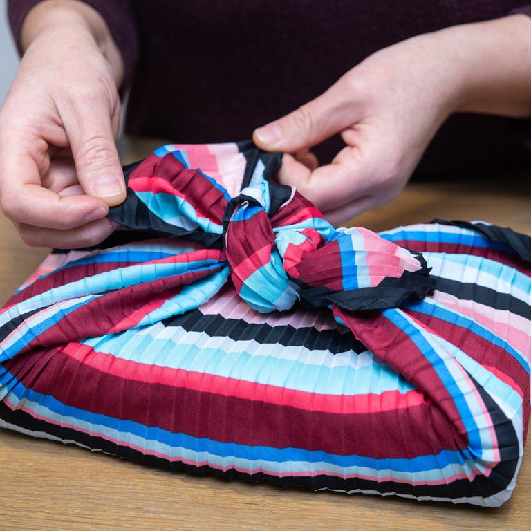 Eine Frau wickelt ein Geschenk mit der japanischen Furoshiki-Technik in ein Tuch ein 