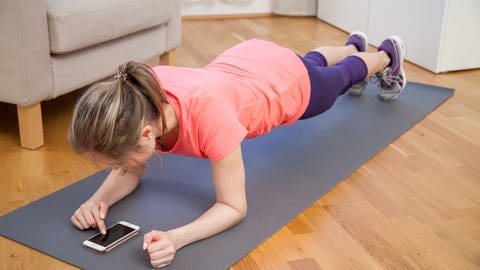 Eine Frau trainiert in ihrer Wohnung mithilfe einer Fitness App auf ihrem Smartphone (Foto: picture-alliance / Reportdienste, Christin Klose)