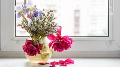 Ein Blumenstrauß steht auf einem Fensterbrett und beginnt zu verwelken.