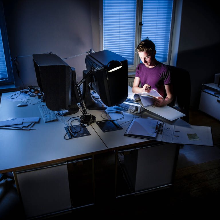 Ein Mann arbeitet nachts in einem Büro an einem Computer, er ist überlastet.