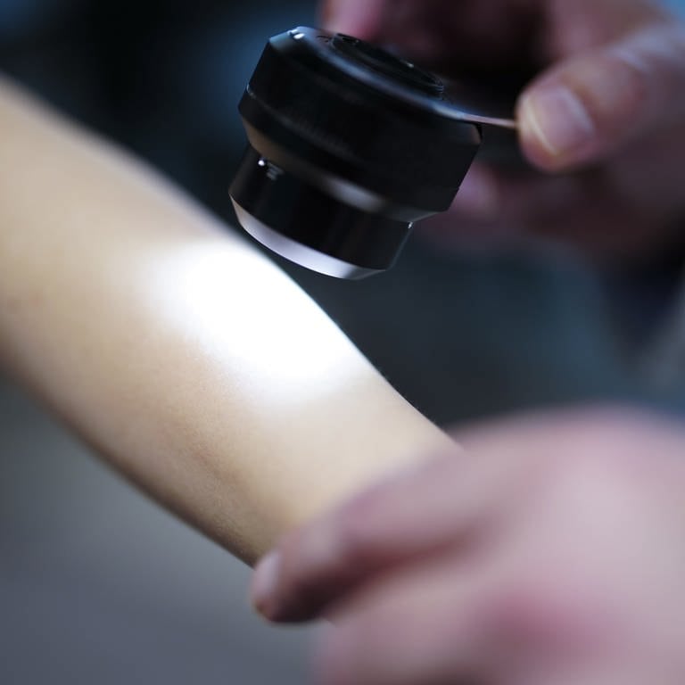 Ein Hautarzt untersucht bei einer Krebsvorsorgeuntersuchung eine Patientin mit einem Auflichtmikroskop.