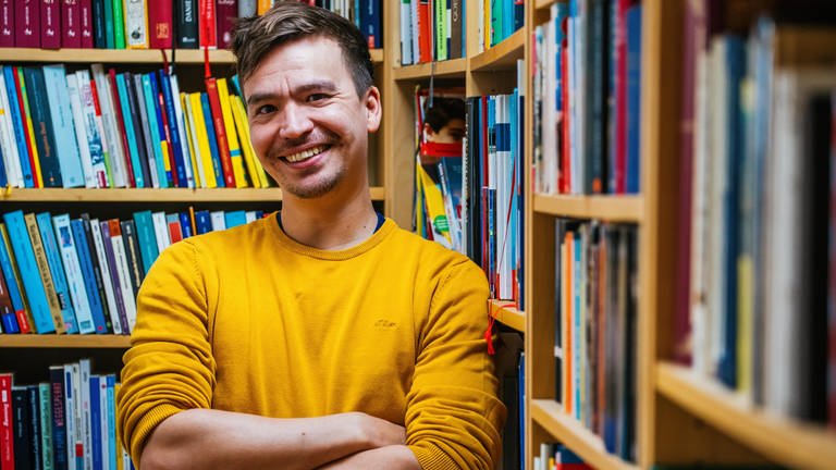 Gymnasiallehrer und Bildungsinfluencer Bob Blume steht lächelnd vor Bücherregalen