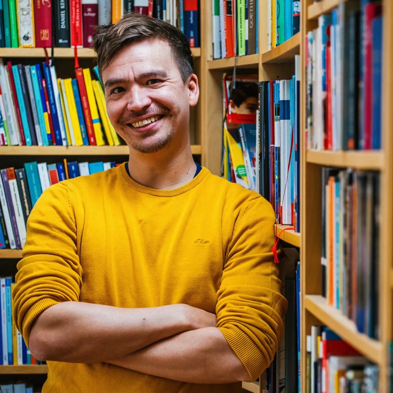 Gymnasiallehrer und Bildungsinfluencer Bob Blume steht lächelnd vor Bücherregalen