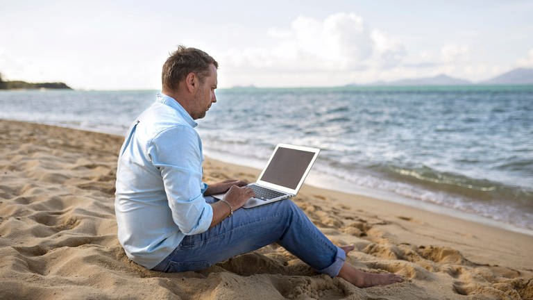 Mann sitzt mit einem Laptop am Strand (Foto: picture-alliance / Reportdienste, picture alliance / Bildagentur-online/Blend Images | Blend Images/Valeriya Tikhonova)