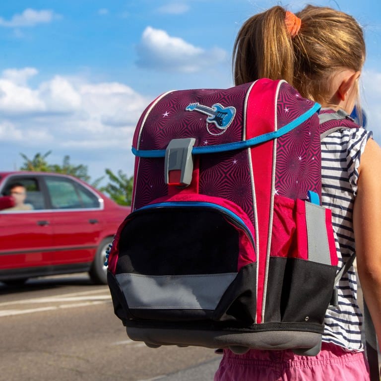 Ein Mädchen mit Ranzen läuft zur Schule, ein Auto fährt vorbei. Kinder sollten auf ihrem Schulweg möglichst nicht allein laufen.