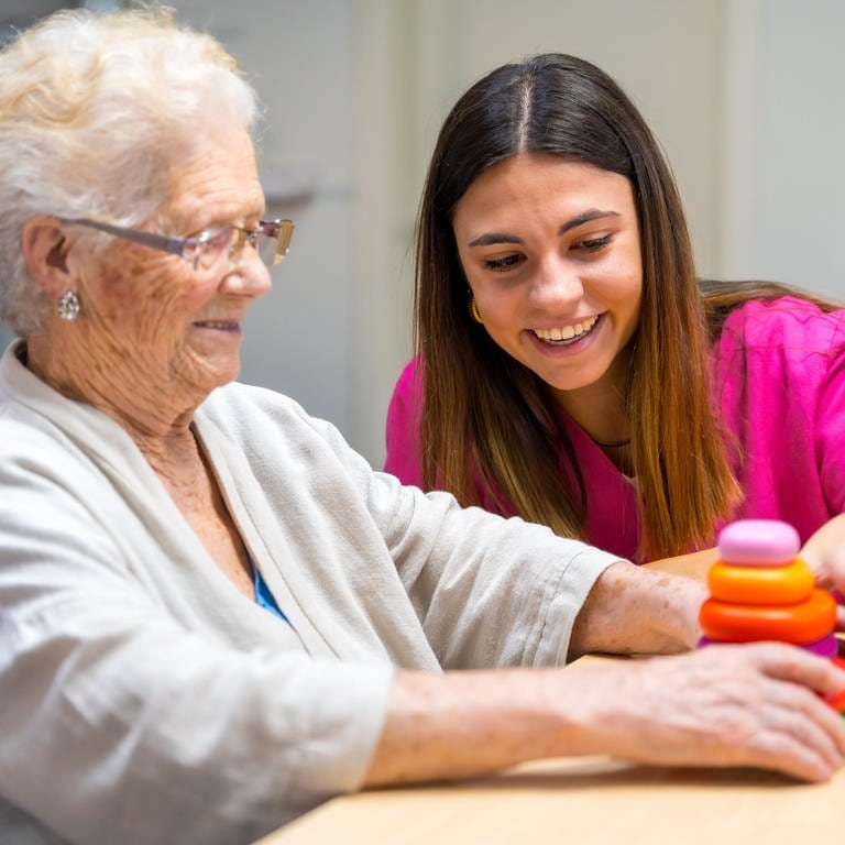 Eine ältere Frau und eine Krankenschwester spielen ein Brettspiel in einem Pflegeheim