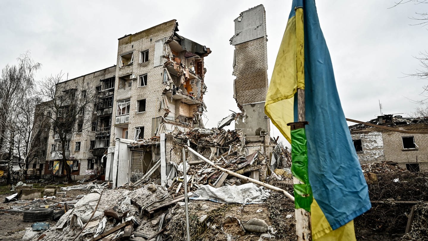 Eine ukrainische Flagge steht vor einem zerstörten Wohnhaus in Orikhiv, im Südosten der Ukraine. (Januar 2024) (Foto: picture-alliance / Reportdienste, picture alliance / Photoshot | Dmytro Smolienko / Avalon)