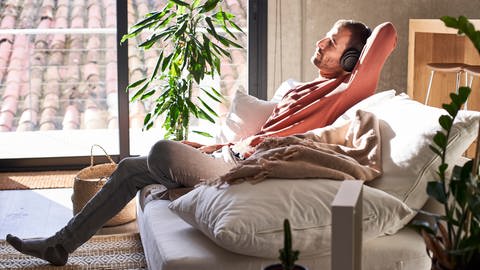Ein Mann trägt Kopfhörer und entspannt auf einem Sofa.