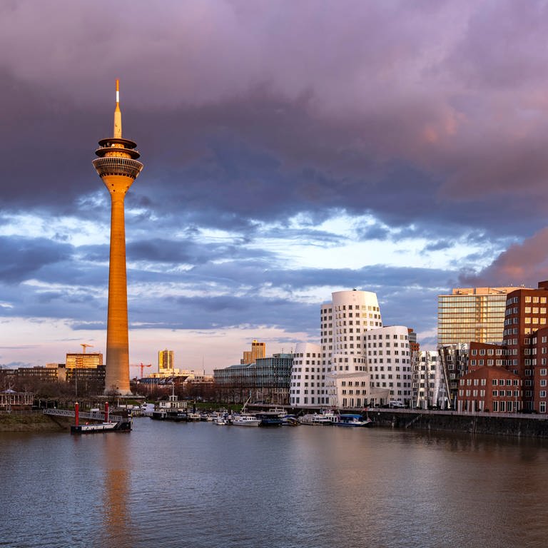 Neuer Zollhof am Medienhafen und der Rheinturm in Düsseldorf bei Sonnenuntergang. Düsseldorf ist nicht nur eine Mode- und Kunststadt, sondern auch die Heimat der Toten hosen, von Westernhagen, Doro Pesch oder Kraftwerk.