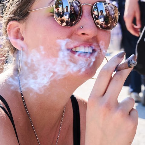 Junge Frau mit Sonnenbrille raucht einen Joint. Ab 1. April ist der Konsum und Besitz von Cannabis in bestimmten Mengen erlaubt. | Was bringt die Teil-Legalisierung von Cannabis? (Foto: picture-alliance / Reportdienste, Annette Riedl)