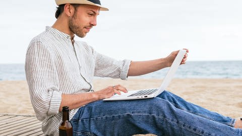 Mann mit Laptop sitzt am Strand