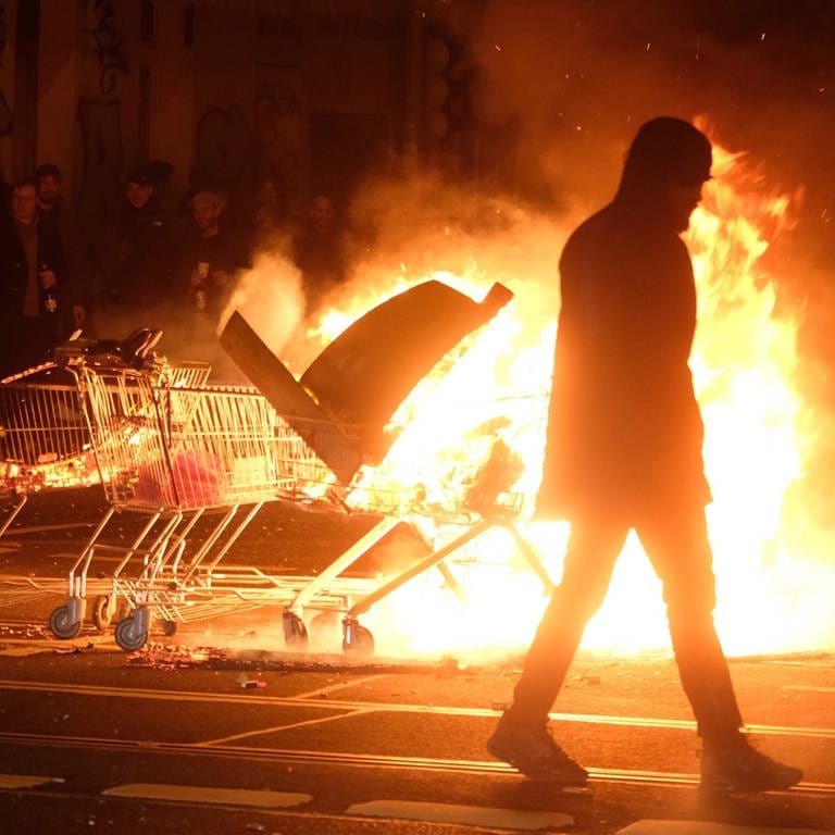 Ein Mann geht an Einkaufwagen mit brennenden Gegenständen vorbeit. Im Osten von Berlin ist es in der Neujahrsnacht zu Ausschreitungen gekommen.