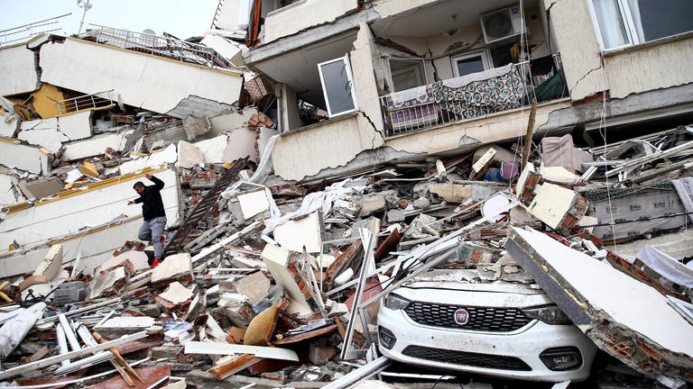 Erdbeben in der Türkei und Syrien: ein Mann auf dem Schuttberg eines zerstörten Hauses. In SWR1 Leute erzählt Pamela Orgeldinger von Care Deutschland, wie wichtig - und wie schwierig - schnelle Hilfe für die Erdbebenopfer jetzt ist.