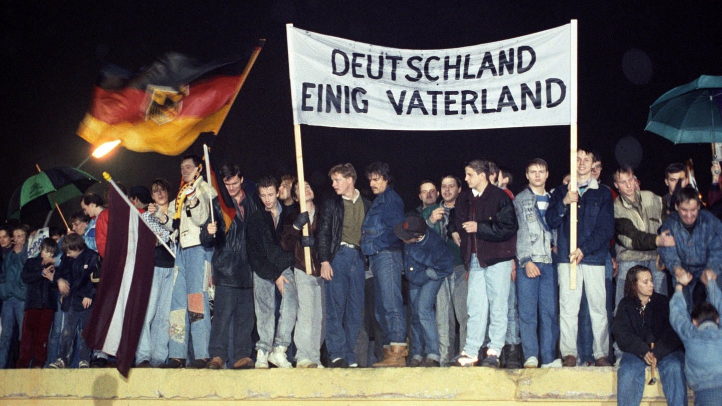 Jahrzehnte nach der Wiedervereinigung ist Deutschland gespalten, sagt Germanist Dirk Oschmann: Westdeutschland blicke auf Ostdeutschland, die ehemalige DDR, herab. Dabei fing alles so gut an: Mit der Deutschlandfahne und einem Transparent 