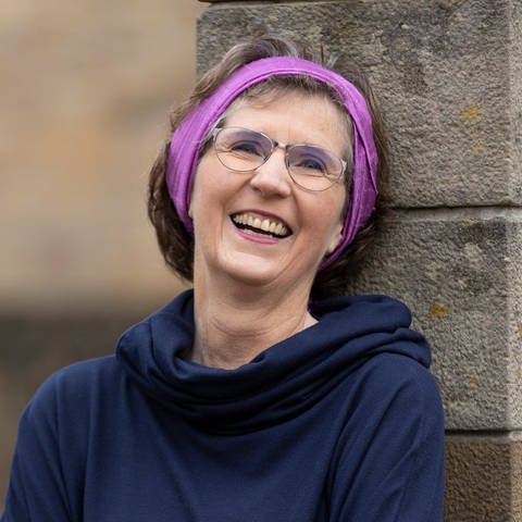Schriftstellerin Lea Söhner spricht in SWR1 Leute über Religion, Liebe, Sexualität, Tod und Abschied. Auf dem Foto trägt sie ein pinkes Stirnband in den Haaren und lehnt sich mit verschränkten Armen an eine Steinmauer. (Foto: privat)