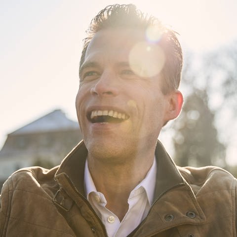 Wissenschaftsjournalist Bas Kast lacht, im Hintergrund scheint die Sonne. In SWR1 Leute spricht der Erfolgsautor von "Ernährungskompass" darüber, wie man sein inneres Gleichgewicht finden kann. Das verrät er in seinem Buch "Kompass für die Seele". (Foto: Mike Meyer)