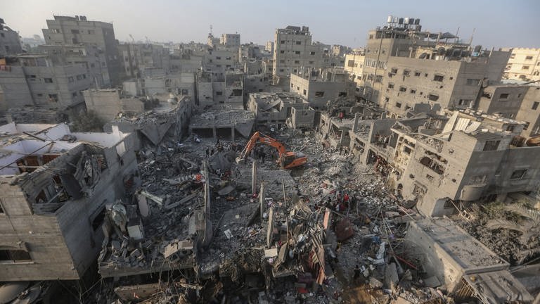 Ein Bagger räumt Trümmer weg, während Menschen nach israelischen Luftangriffen in Gebäuden nach Überlebenden suchen.