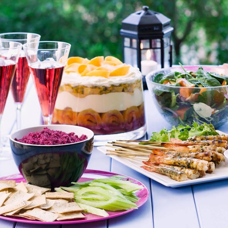 Gedeckter Tisch im Garten mit Garnelenspiessen, Rote-Bete-Dip, Spinatsalat und Trifle