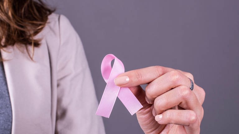 Rosa Schleife in der Hand einer Frau zur Unterstützung von Brustkrebs