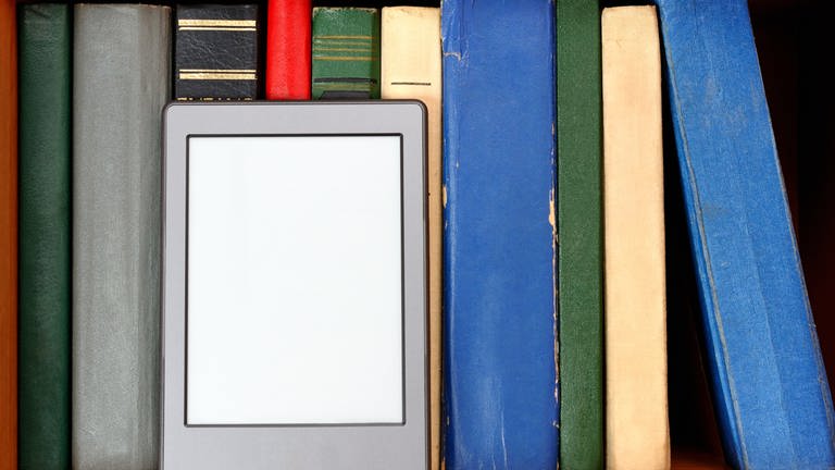 Ebook-Reader vor einer bunten Bücherwand (Foto: IMAGO, IMAGO / agefotostock)