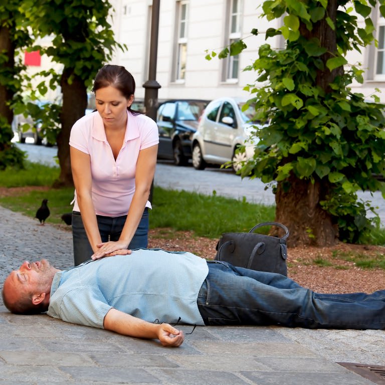 Ein Mann mit Herzinfarkt oder Schlaganfall auf der Strasse, Frau versucht Wiederbelebung (Foto: IMAGO, IMAGO / McPHOTO)