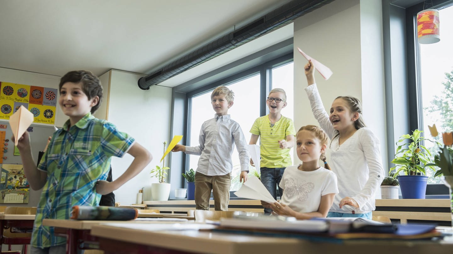 Schulkinder spielen mit Papierfliegern im Klassenzimmer (Foto: IMAGO, IMAGO / Cavan Images)