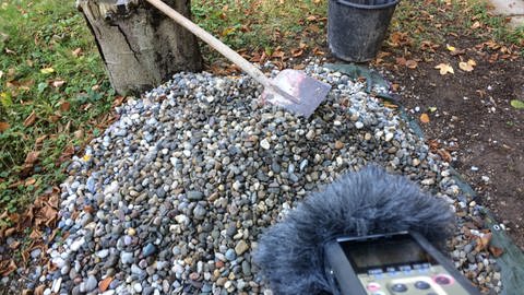 Ein kleiner Kiesberg in einem grünen Garten, dabei Schaufel und ein digitales Aufnahmegerät (Foto: SWR)