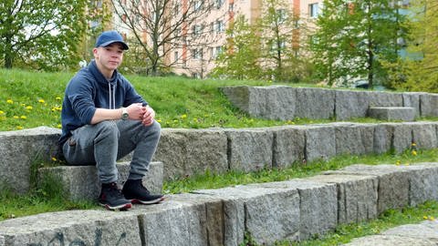 Ein Jugendlicher sitzt auf einer Steintreppe in einer Parkanlage (Foto: Massimo Maio)