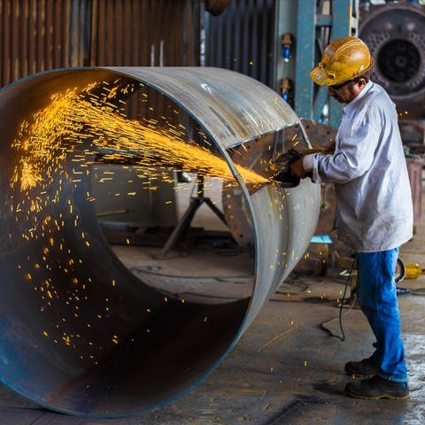Fabrikarbeiter bei der Arbeit an einen großes Metallrohr. Funken schlagen (Foto: Foto von Ahsanization | Unsplash )