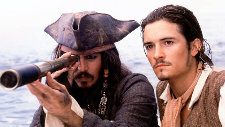 Johnny Depp schaut als Captain Jack Sparrow durch ein Fernglas. Neben ihm Orlando Bloom. (Foto: dpa Bildfunk, picture-alliance / Mary Evans Picture Library)