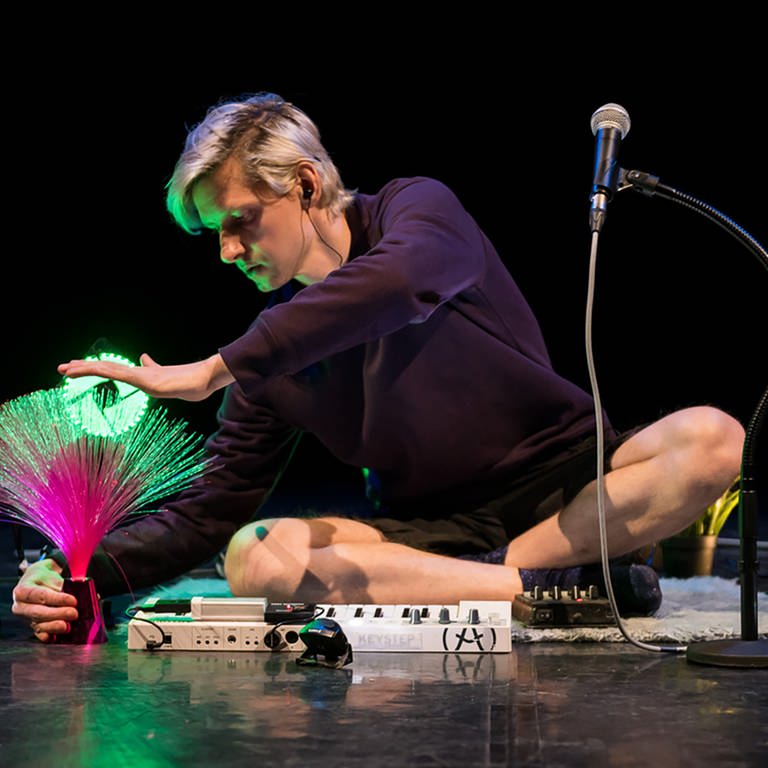 Mann in Schneidersitz auf Bühne und berührt Glasfaserleuchte (Foto: SWR, E-Werk Freiburg - Marc Doradzillo)