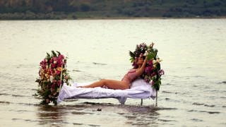 Atme - Eine Frau liegt auf einem Bett im See (Foto: imago images, imago)