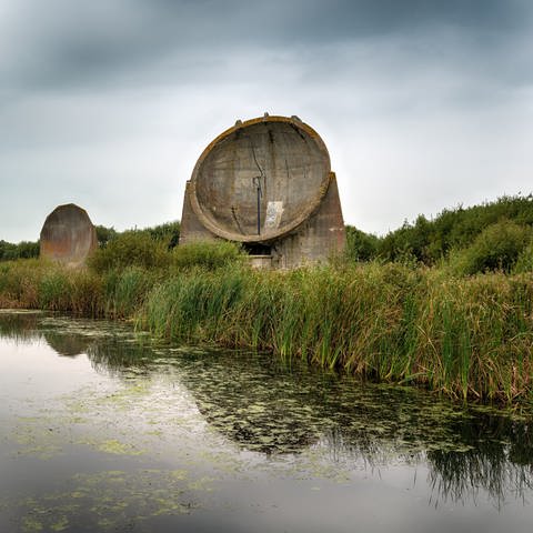 zwei große akustische Parabolspiegel aus Beton in einer Graslandschaft mit Tümpel (Foto: IMAGO, CSP_ziggyzag)